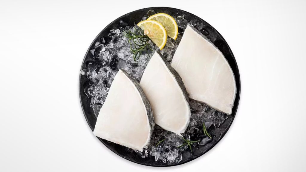 patagonian toothfish steak with ice and lemon on black plate